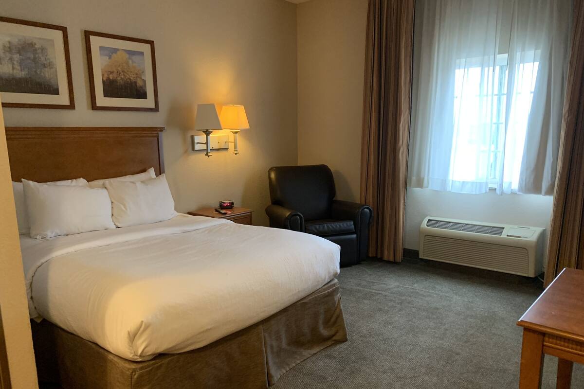 Een hotelkamer met een groot bed, een stoel, een bureau, een lamp en een raam met gordijnen.