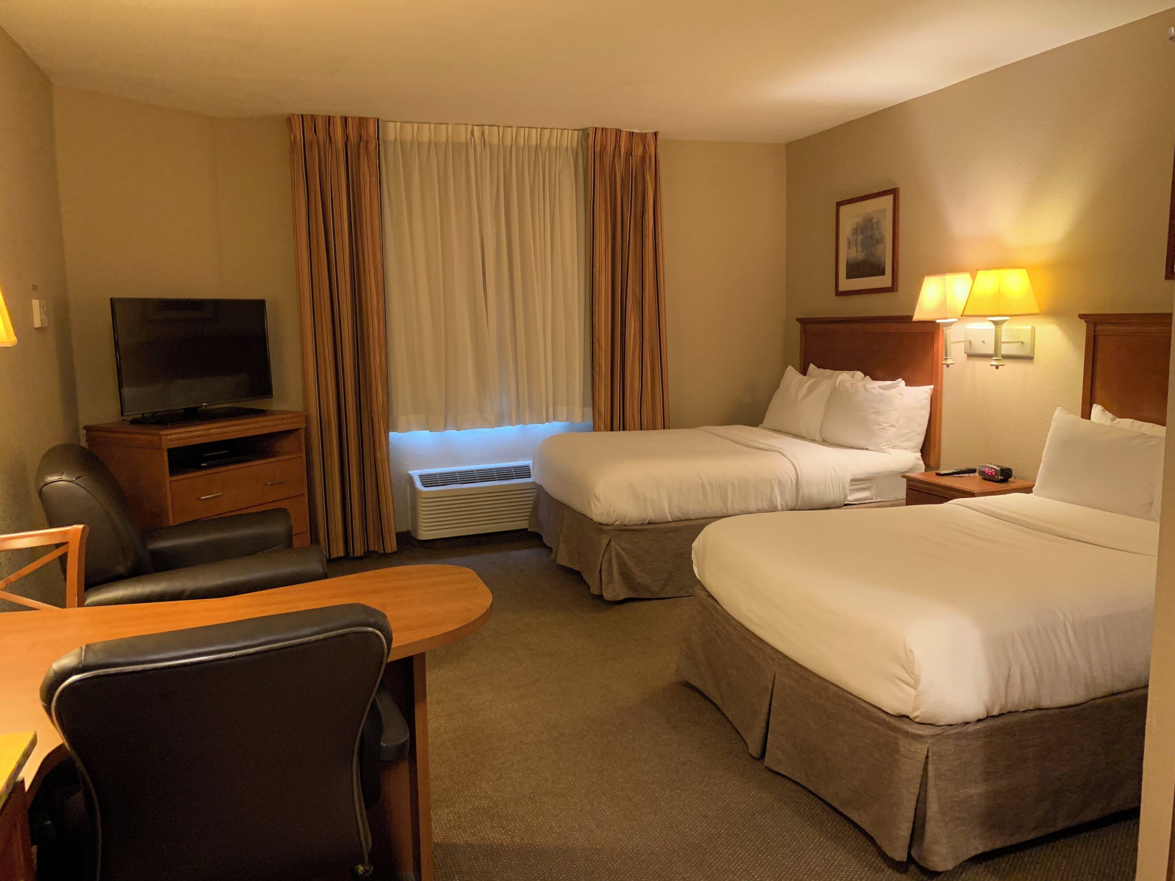 A hotel room with two beds, a desk, a chair, a television, and a lamp.