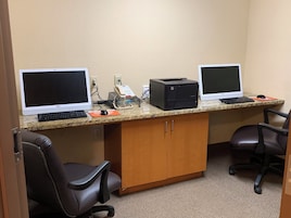 A workspace with two desktop computers, a printer, and office chairs.