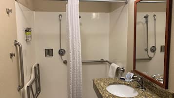 A bathroom with a shower, grab bars, a sink, and a mirror.