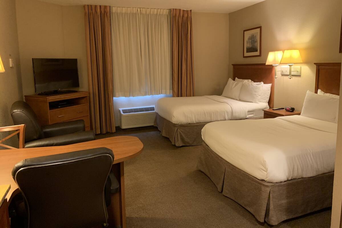 Een hotelkamer met twee bedden, een bureau met stoel, een televisie, een verwarming en een lamp.