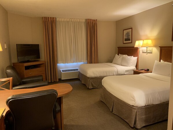 A hotel room with two beds, a desk with a chair, a television, a heater, and a lamp. - Candlewood Suites Jonesboro by IHG (Jonesboro)