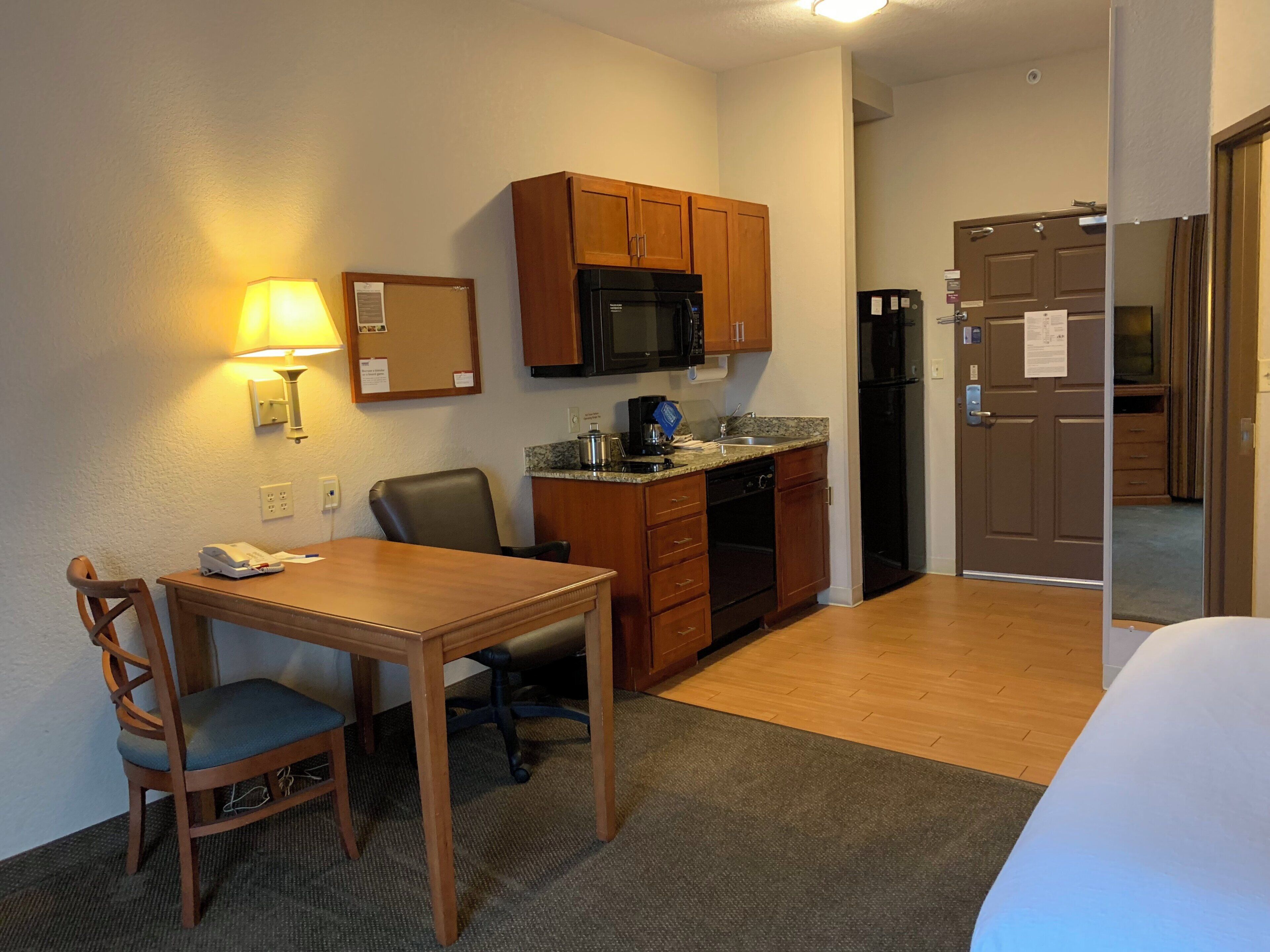 Habitación de hotel compacta con kitchenette, zona de comedor con mesa y sillas, microondas y refrigerador.