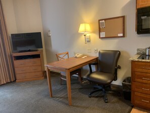 A hotel room with a wooden desk, a chair, a television, a lamp, a telephone, a bulletin board, and a kitchenette. - Candlewood Suites Jonesboro by IHG (Jonesboro)