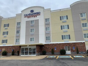 Ein mehrstöckiges Hotel mit einem gut sichtbaren 'CANDLEWOOD SUITES'-Schild, einer Ziegel-Fassade und ausgewiesenen Parkplätzen für Gäste mit Behinderung.