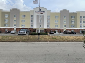 A hotel with a central entrance, multiple floors, and a parking lot with several vehicles.
