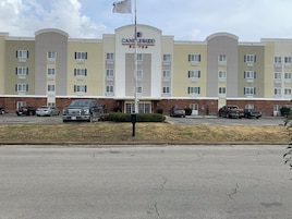 Un hotel con entrada central, varios pisos y un estacionamiento con varios vehículos.