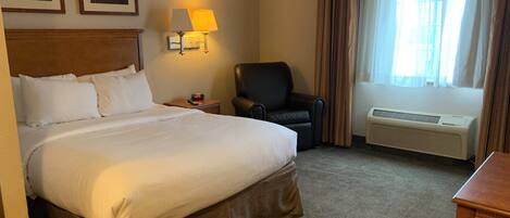 A hotel room with a large bed, a chair, a desk, a lamp, and a window with curtains.