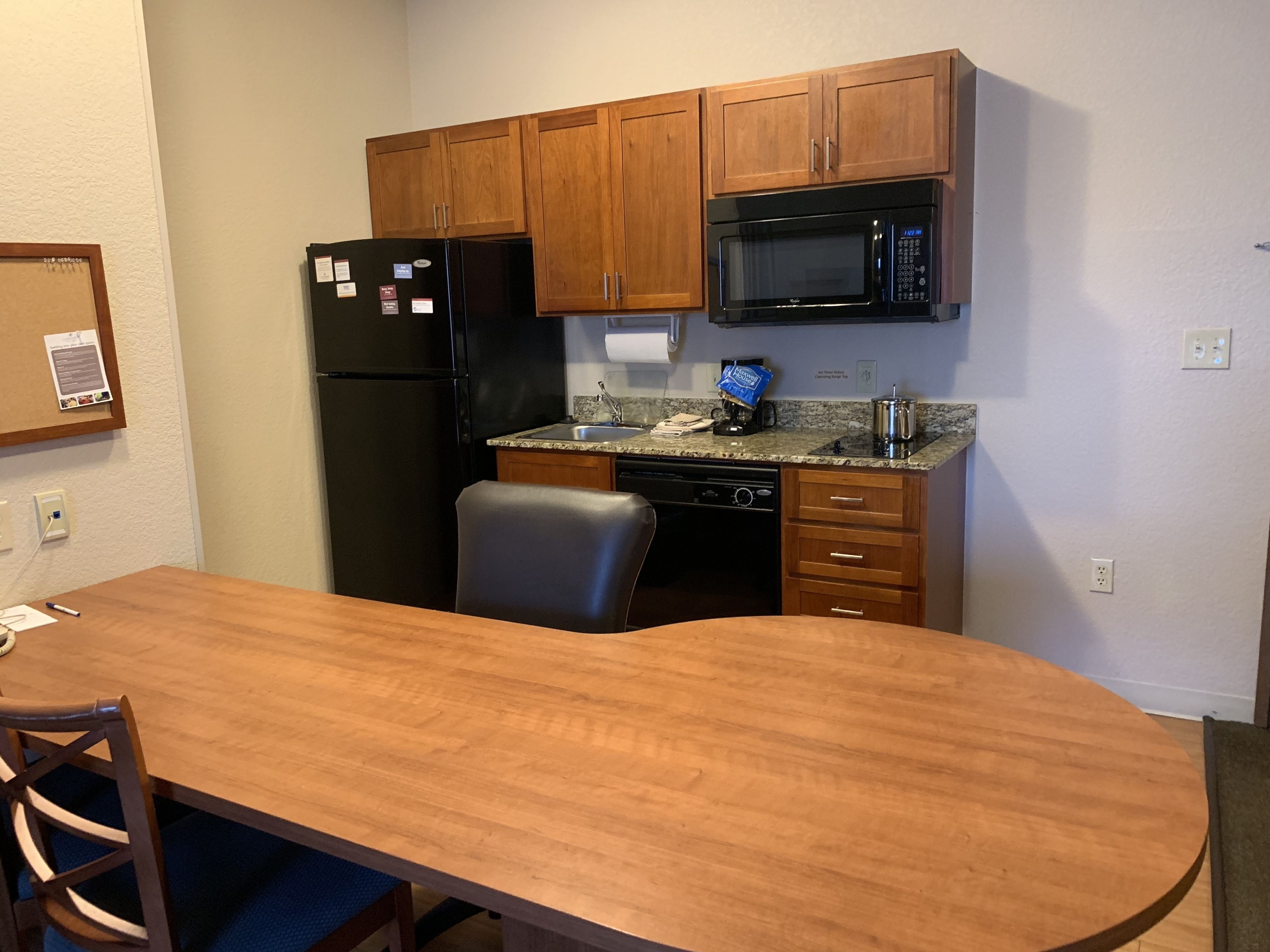 A compact kitchen with wooden cabinets, a black refrigerator, a microwave, and a sink.