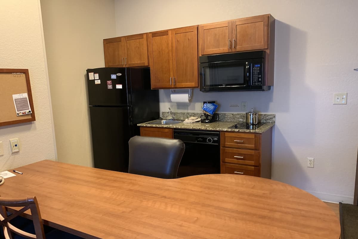 Una cocina compacta con armarios de madera, un refrigerador negro, un microondas y un lavamanos.