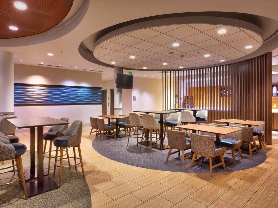 Un restaurant moderne avec des tables rondes et des tabourets de bar, un mur d’accent en bois et un plafond doté d’un éclairage encastré.