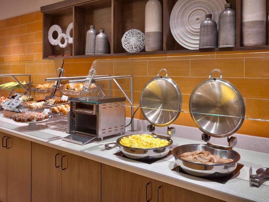 A buffet with various food items, including scrambled eggs, meats, and pastries.