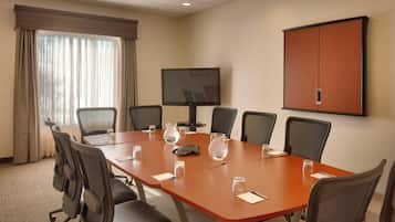 Une salle de conférence avec une longue table, six chaises, un téléviseur et un meuble.