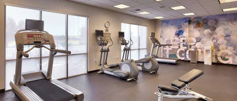 Et fitnesscenter med løbebånd, crosstrainere og bænk.