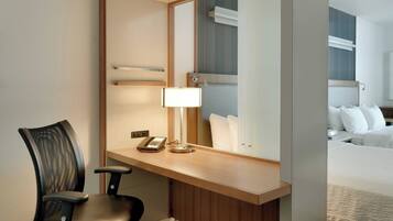A hotel room with a desk, chair, and a large mirror reflecting the bed and a nightstand.