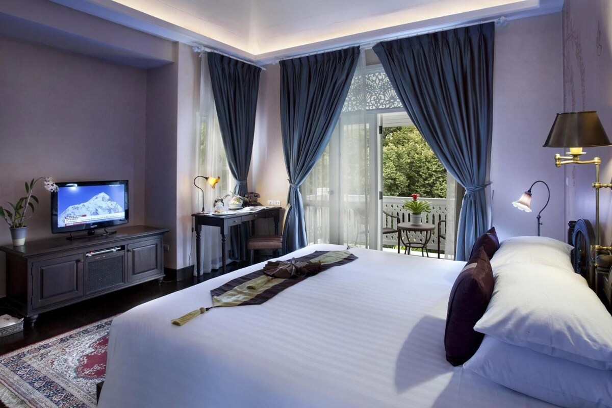 A hotel room with a bed, a desk, a television, and a balcony with a table and chairs.