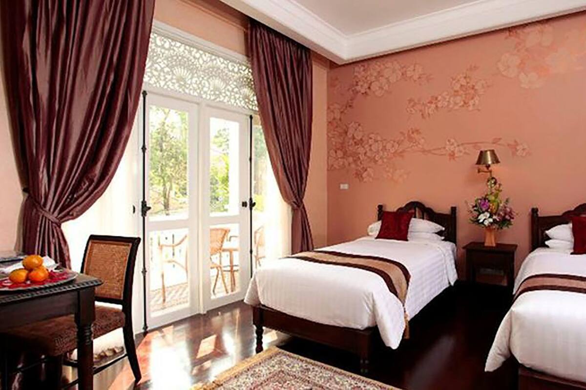Une chambre d’hôtel avec deux lits, une table à manger avec des fruits, et une vue à travers une porte vitrée.