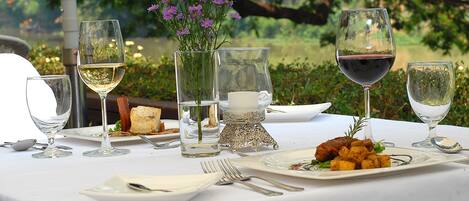 A table set for a meal with wine glasses, plates, cutlery, and a vase with flowers.