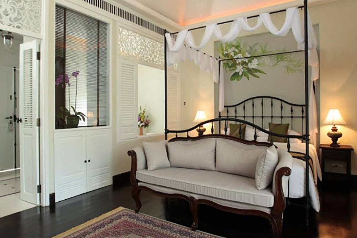 Une chambre à coucher avec un lit à baldaquin, un canapé, un miroir et une fenêtre avec des stores.