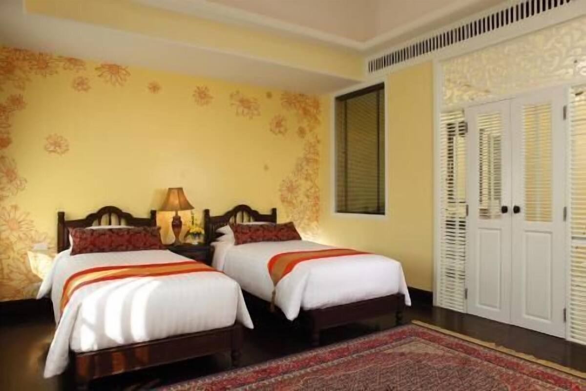 Une chambre d’hôtel avec deux lits, une table de chevet avec une lampe, un grand miroir et une armoire.
