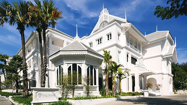 A large, white, two-story building with a symmetrical facade, multiple windows, and a central entrance with a decorative archway.