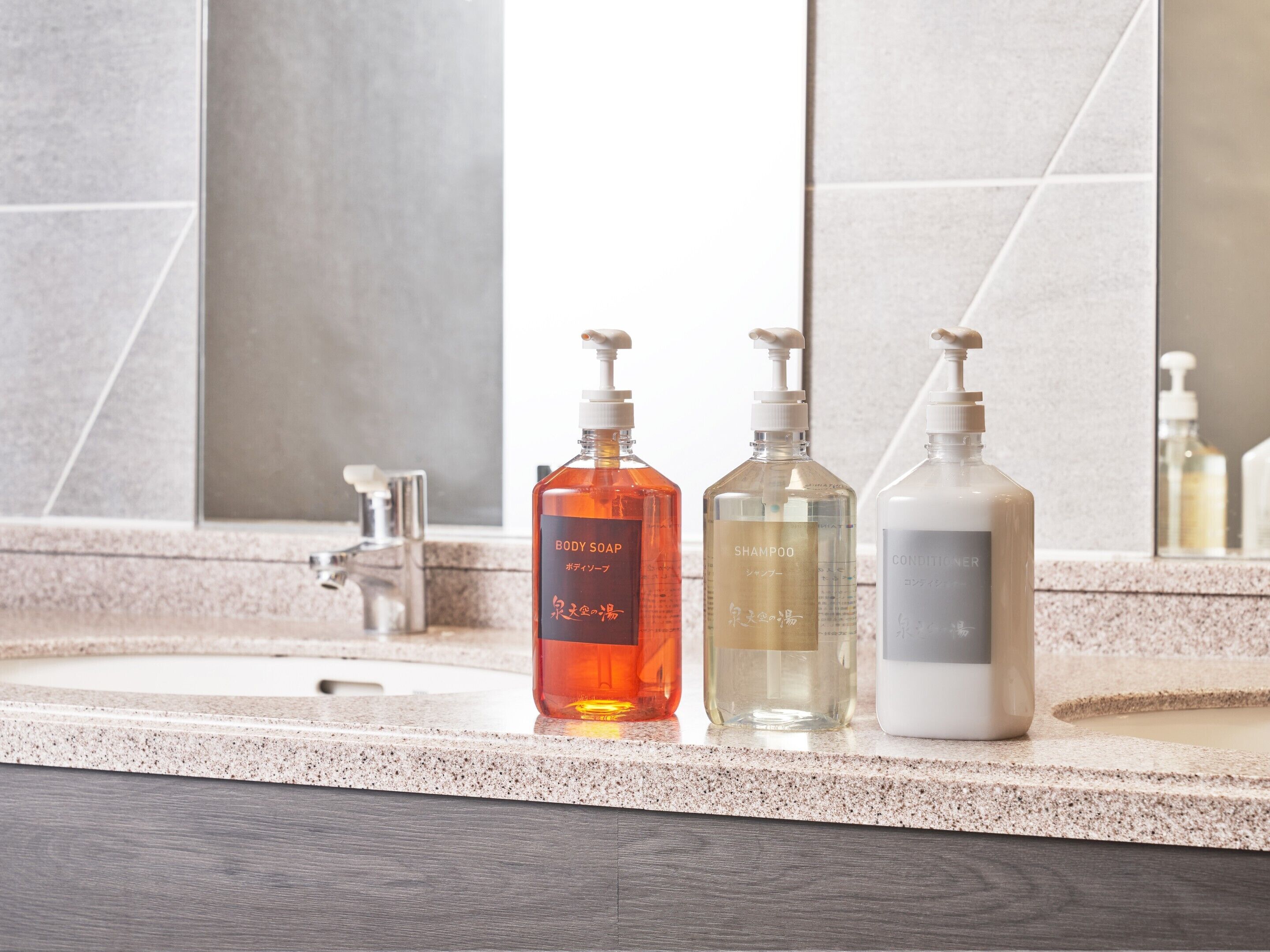 Un baño con encimera de granito y tres botellas de artículos de aseo: jabón corporal, champú y acondicionador.