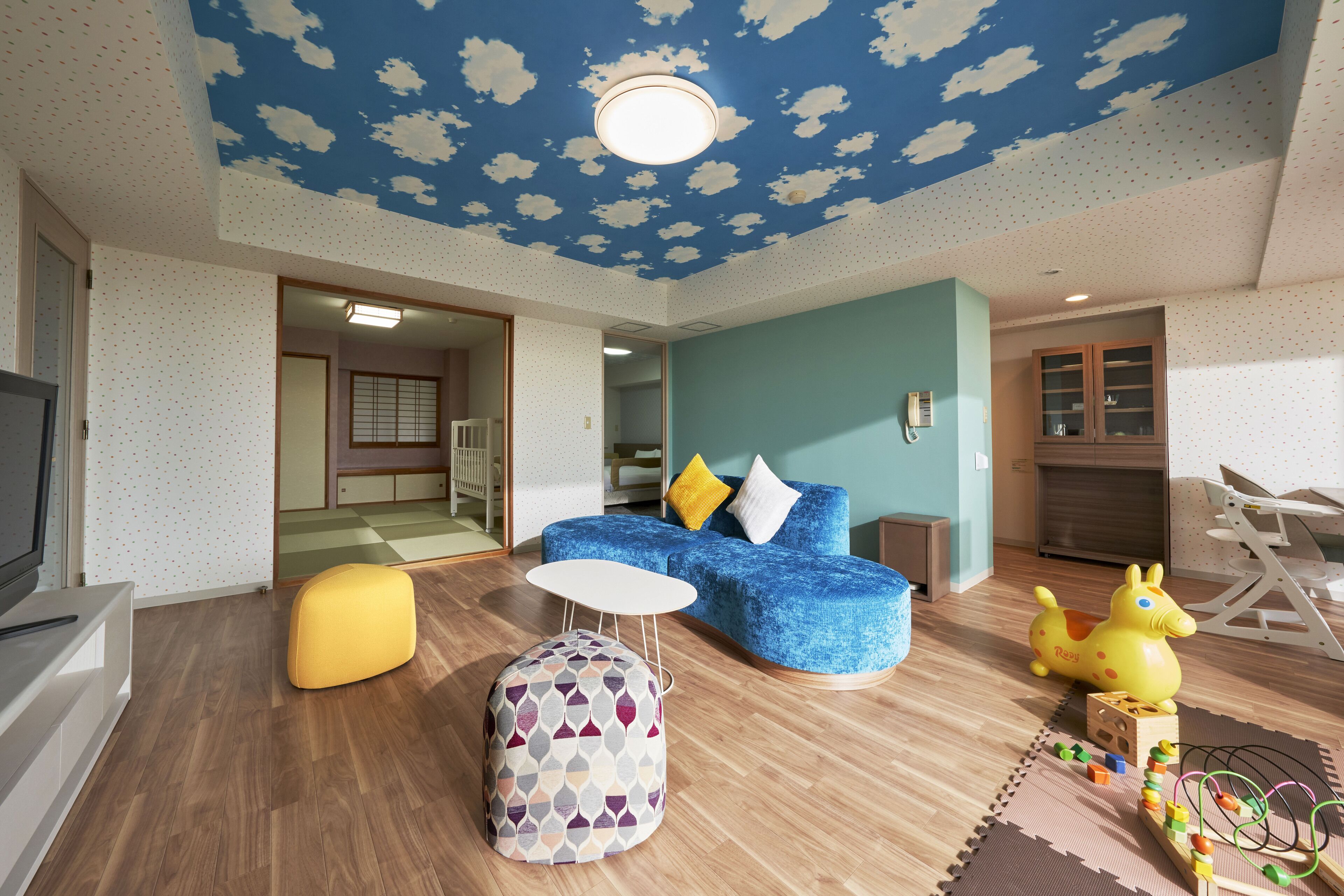 A living room with a blue sofa, a yellow ottoman, and a wooden play table.