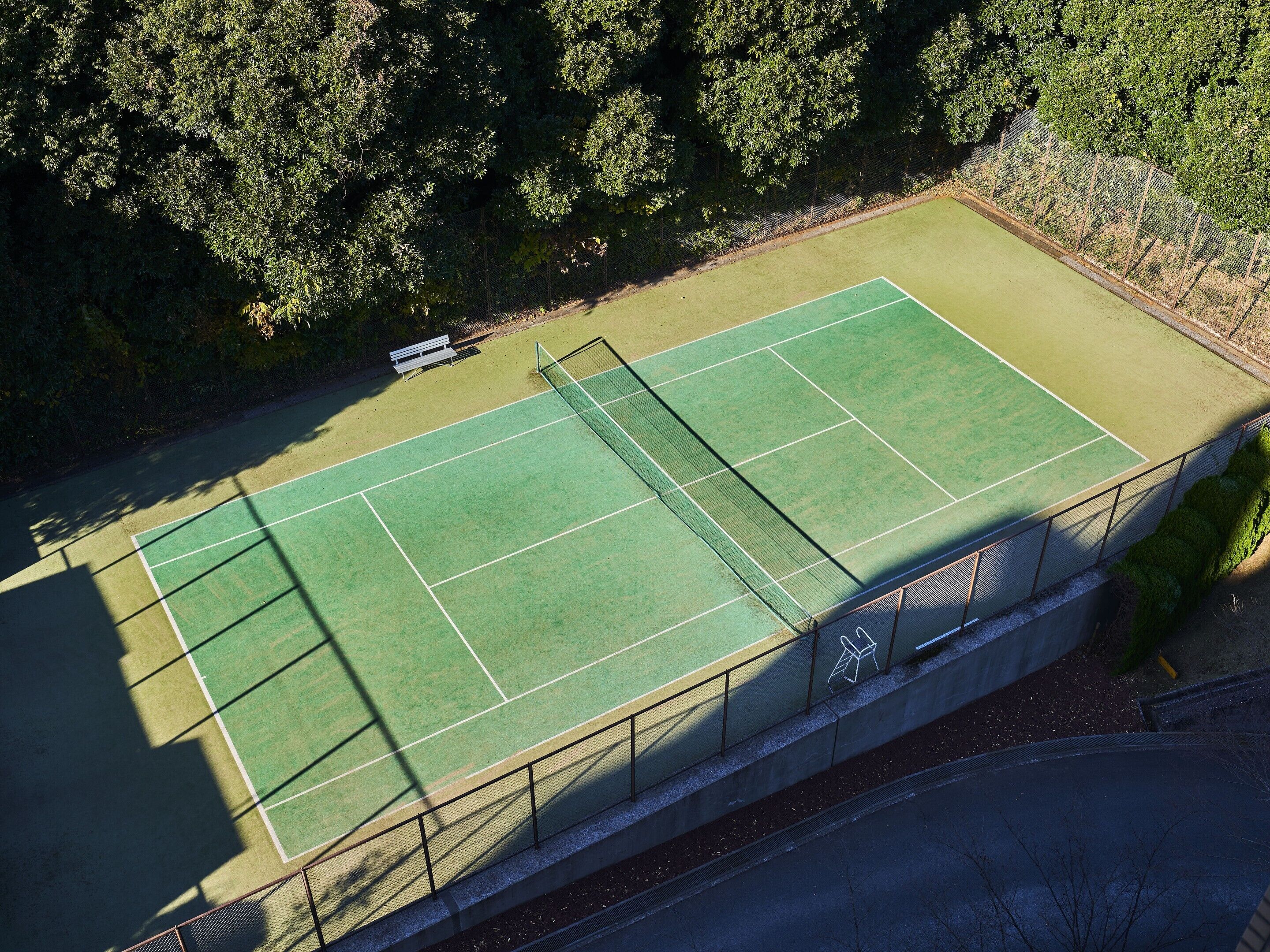 Vue aérienne d’un court de tennis avec une clôture, des arbres et un banc.