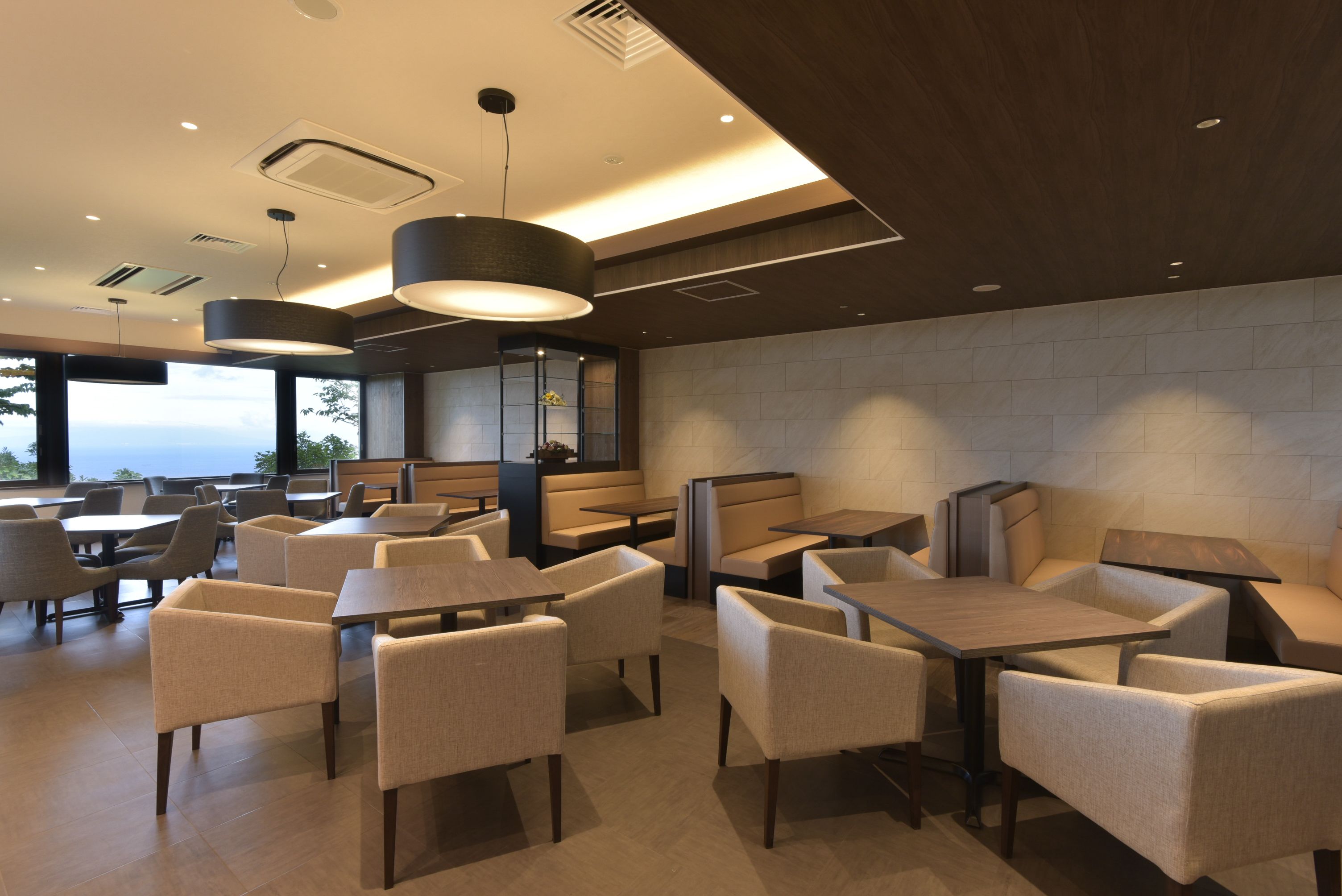 A modern dining area with tables and chairs, recessed lighting, and a view through large windows.