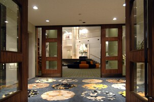 A hotel lobby with a carpeted floor, wooden doors, and a staircase leading to an upper level.