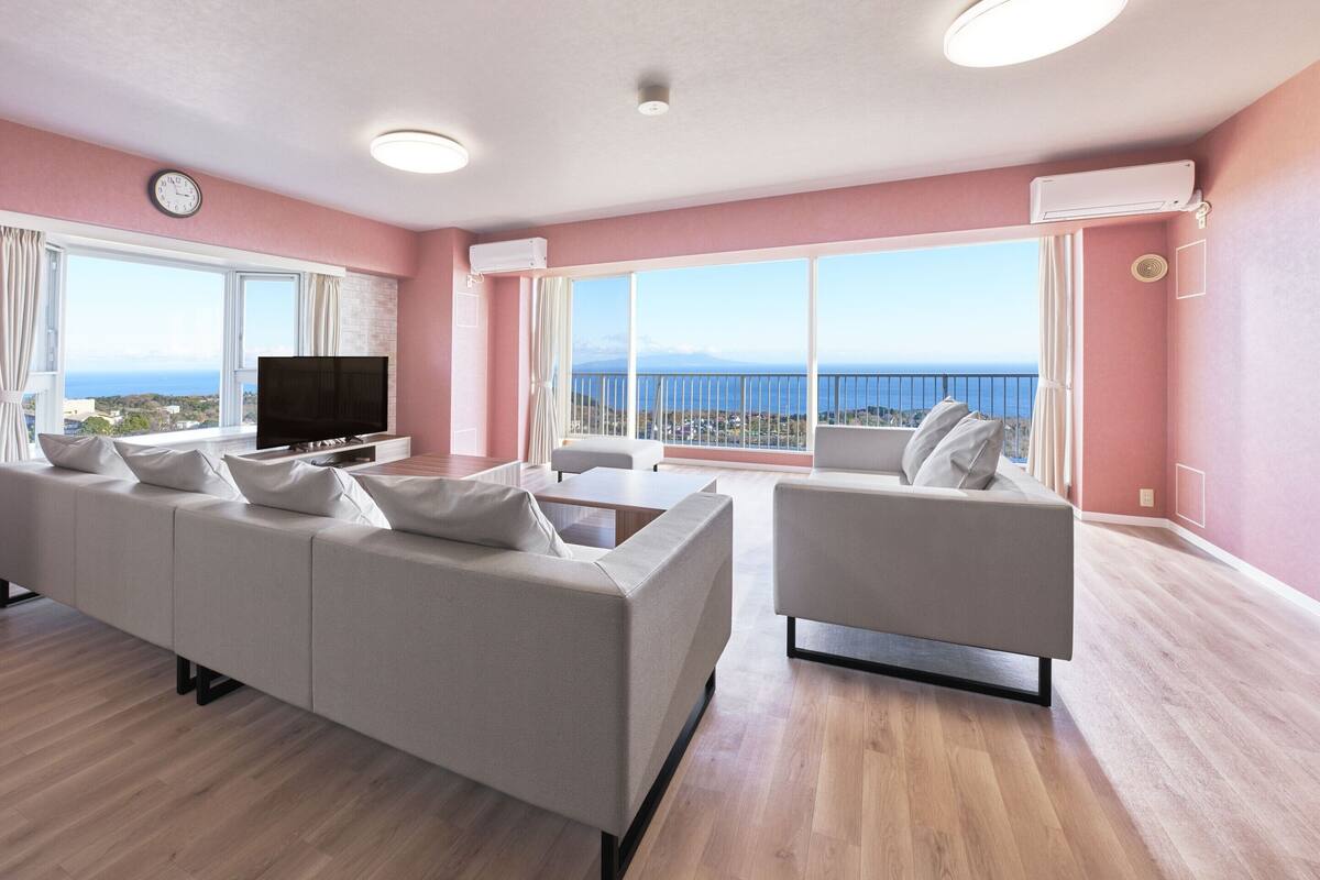 Un salon moderne avec un grand canapé, un fauteuil plus petit, un téléviseur à écran plat et une grande fenêtre donnant sur la mer.