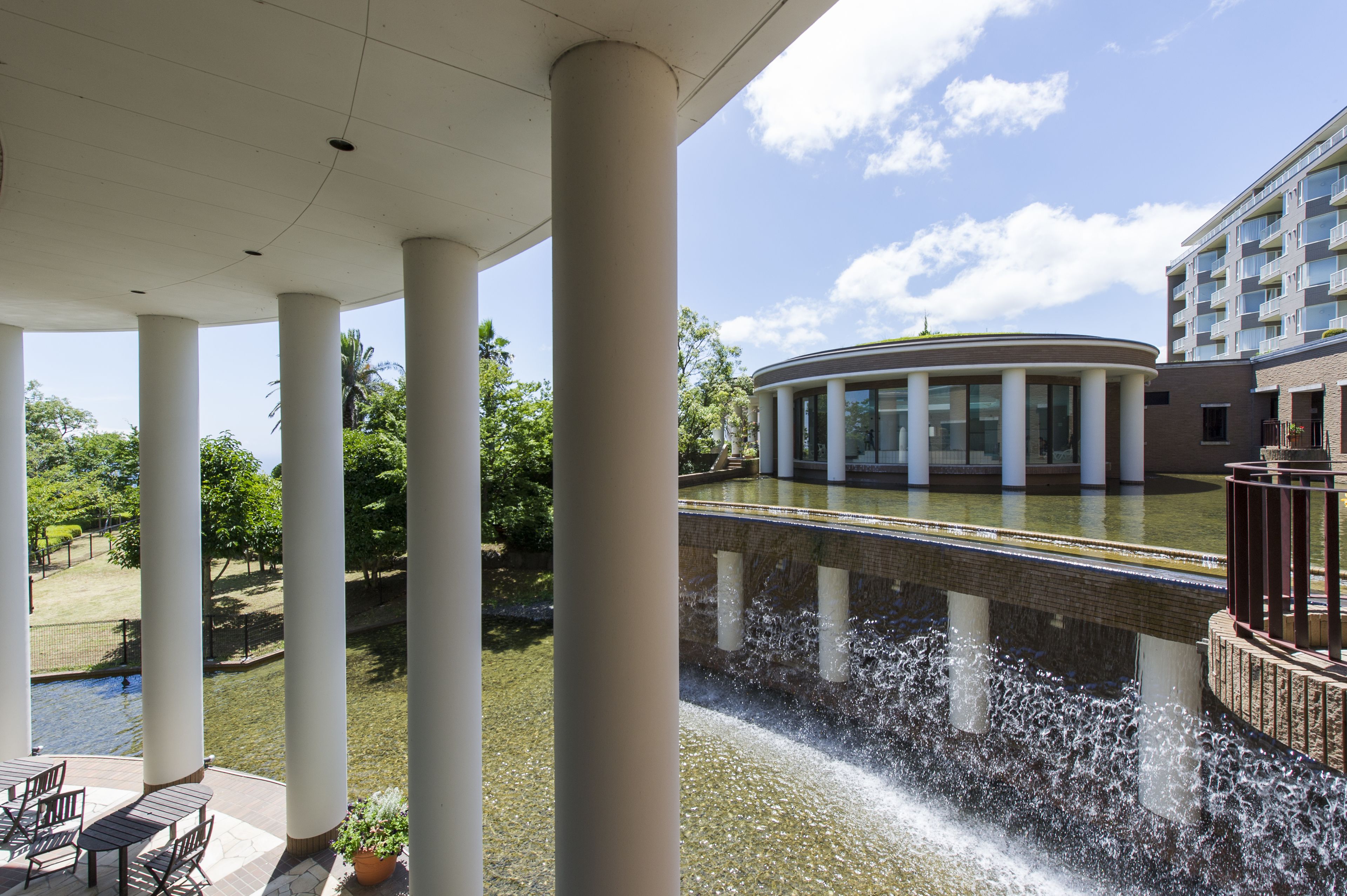 A covered outdoor area with columns, a water feature, and a building with large windows.