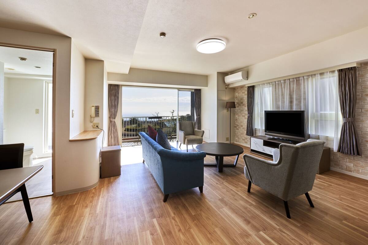 Un salon moderne avec un canapé, des fauteuils, un téléviseur et un balcon offrant une vue agréable.