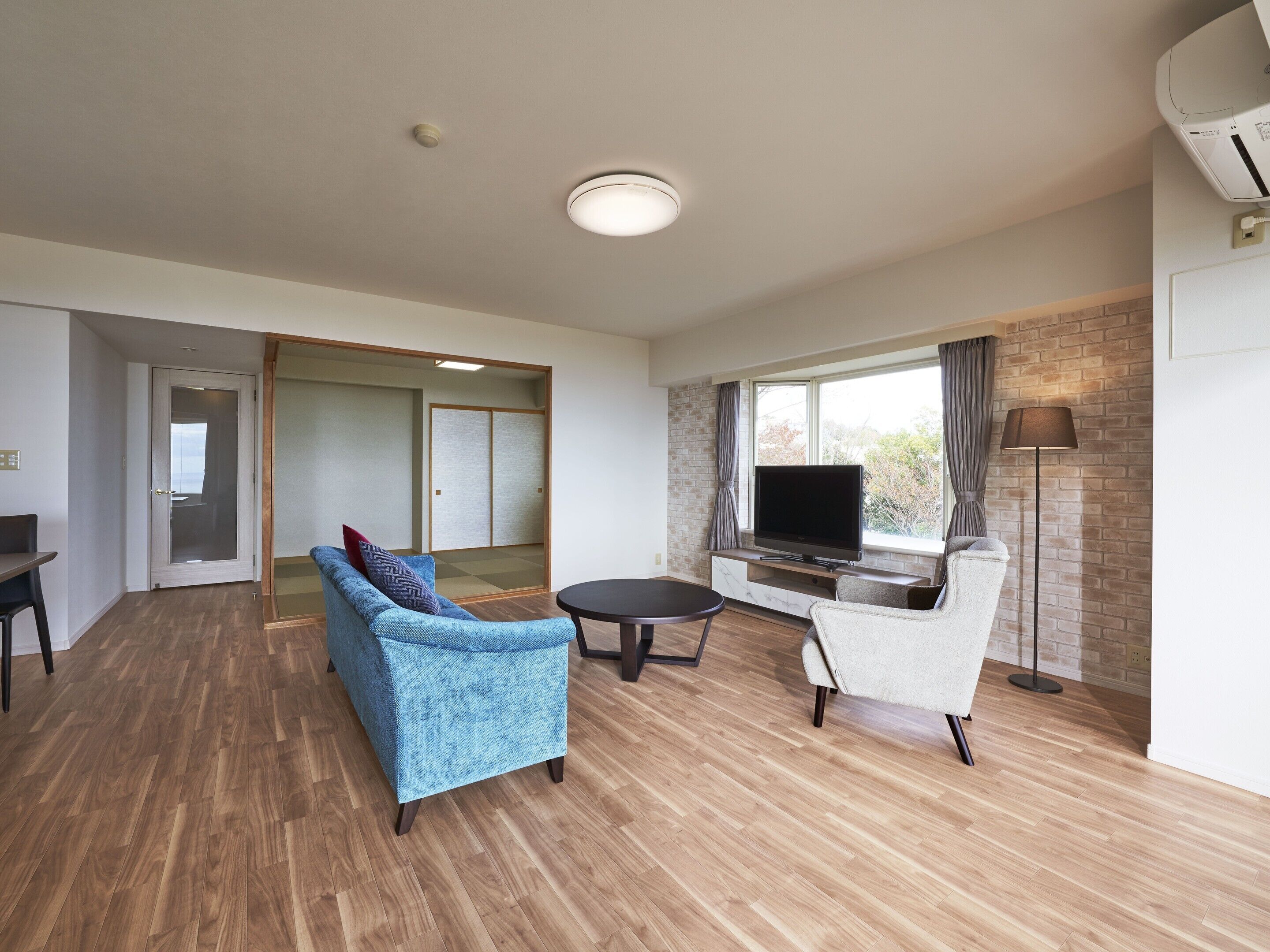 A modern living room with a flat-screen TV, two sofas, a coffee table, and a brick-patterned wall.
