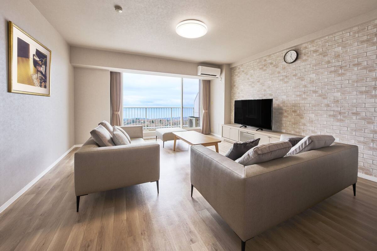Un salon moderne doté d’un grand téléviseur, de deux canapés, d’une table basse et d’un balcon offrant une vue agréable.