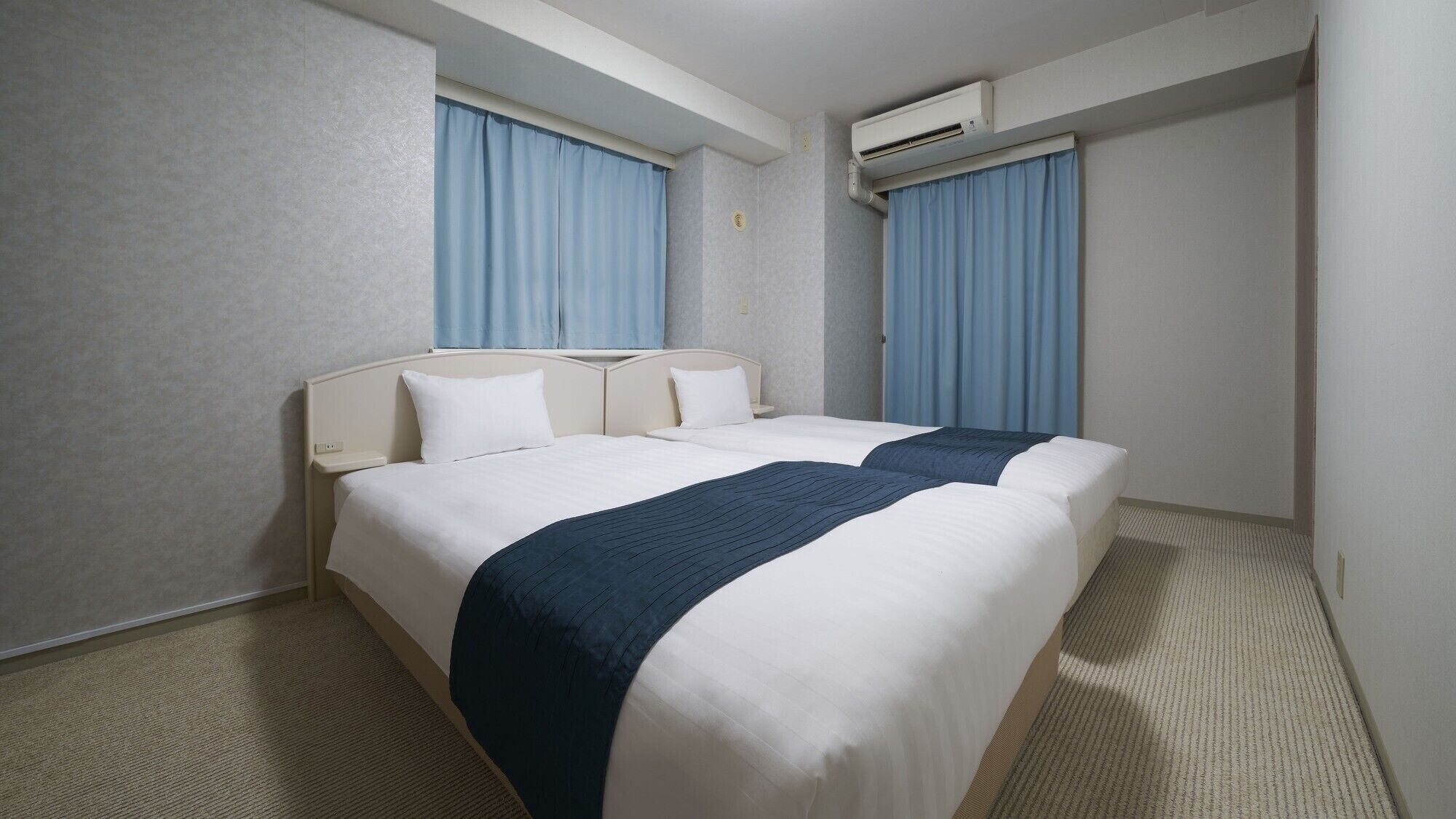 Een hotelkamer met twee bedden, een hoofdeinde, een vloerbedekking en een airconditioning.