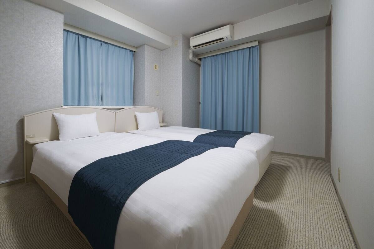 Une chambre d’hôtel avec deux lits, une tête de lit, un sol recouvert de moquette et un appareil de climatisation.