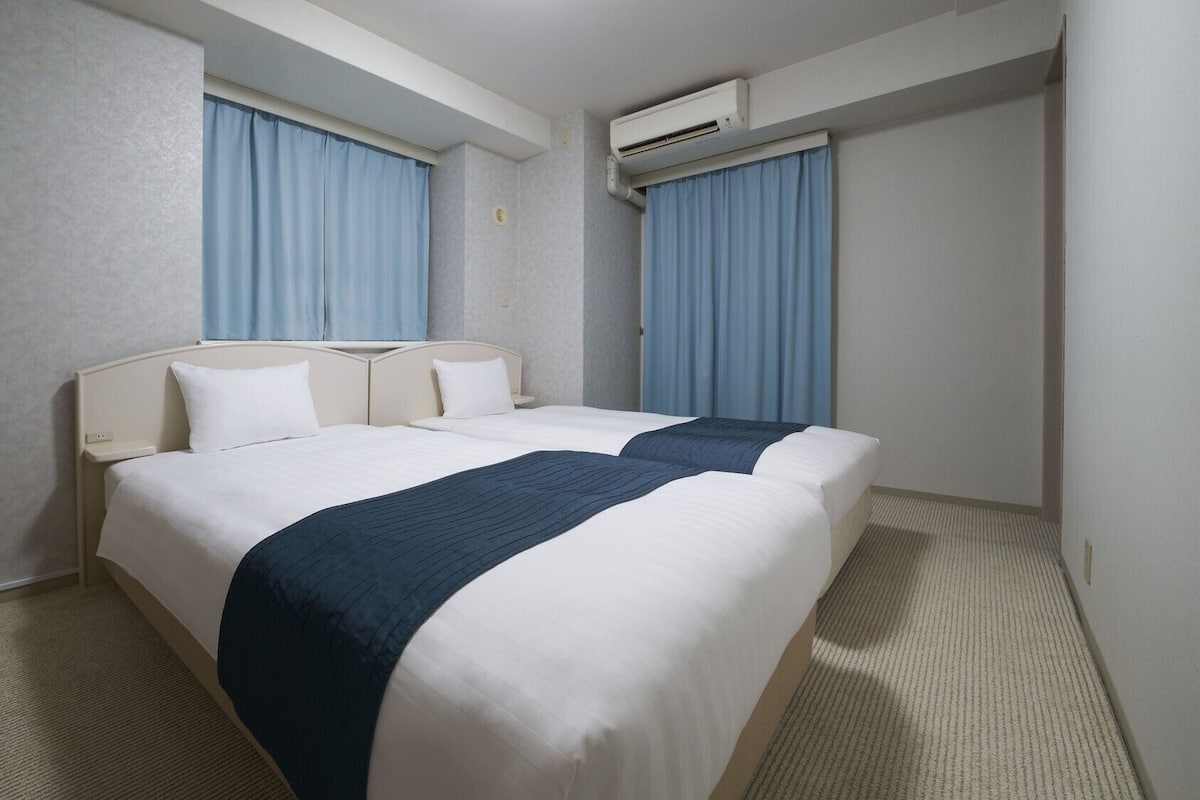Habitación de hotel con dos camas, cabecera, piso alfombrado y equipo de aire acondicionado.