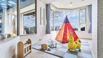 Explore and play in this vibrant playroom with a view of the outdoors, featuring a colorful play tent and a wooden toy chest.