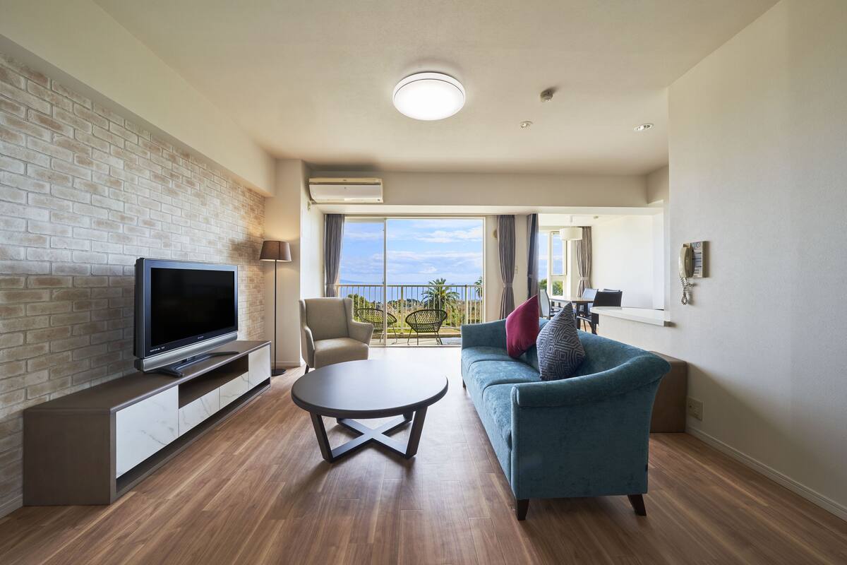 Un salon moderne doté d’un téléviseur à écran plat, d’une table basse ronde, d’un canapé bleu et d’un balcon avec vue.