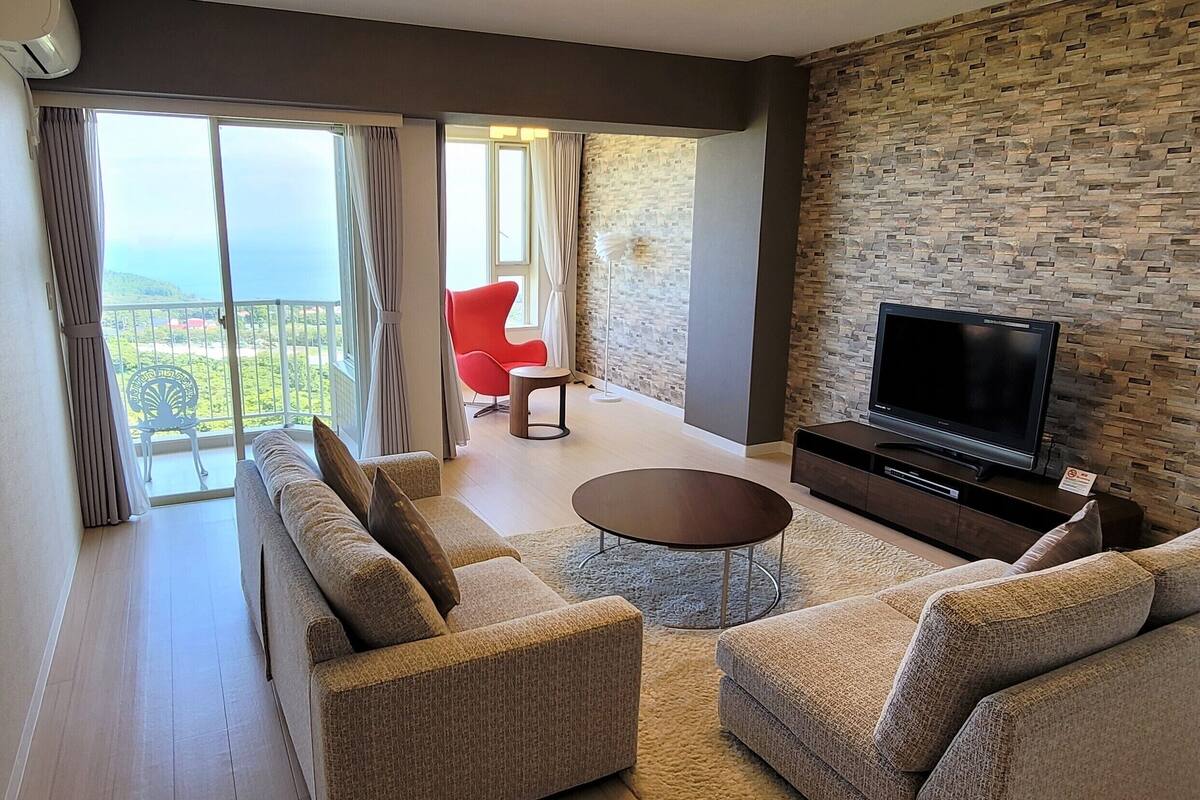 Un salon moderne comprenant un ensemble de canapés, une table basse, un téléviseur à écran plat et un mur à la texture de pierre.