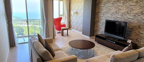 A modern living room with a sofa set, a coffee table, a flat-screen TV, and a stone-textured wall.