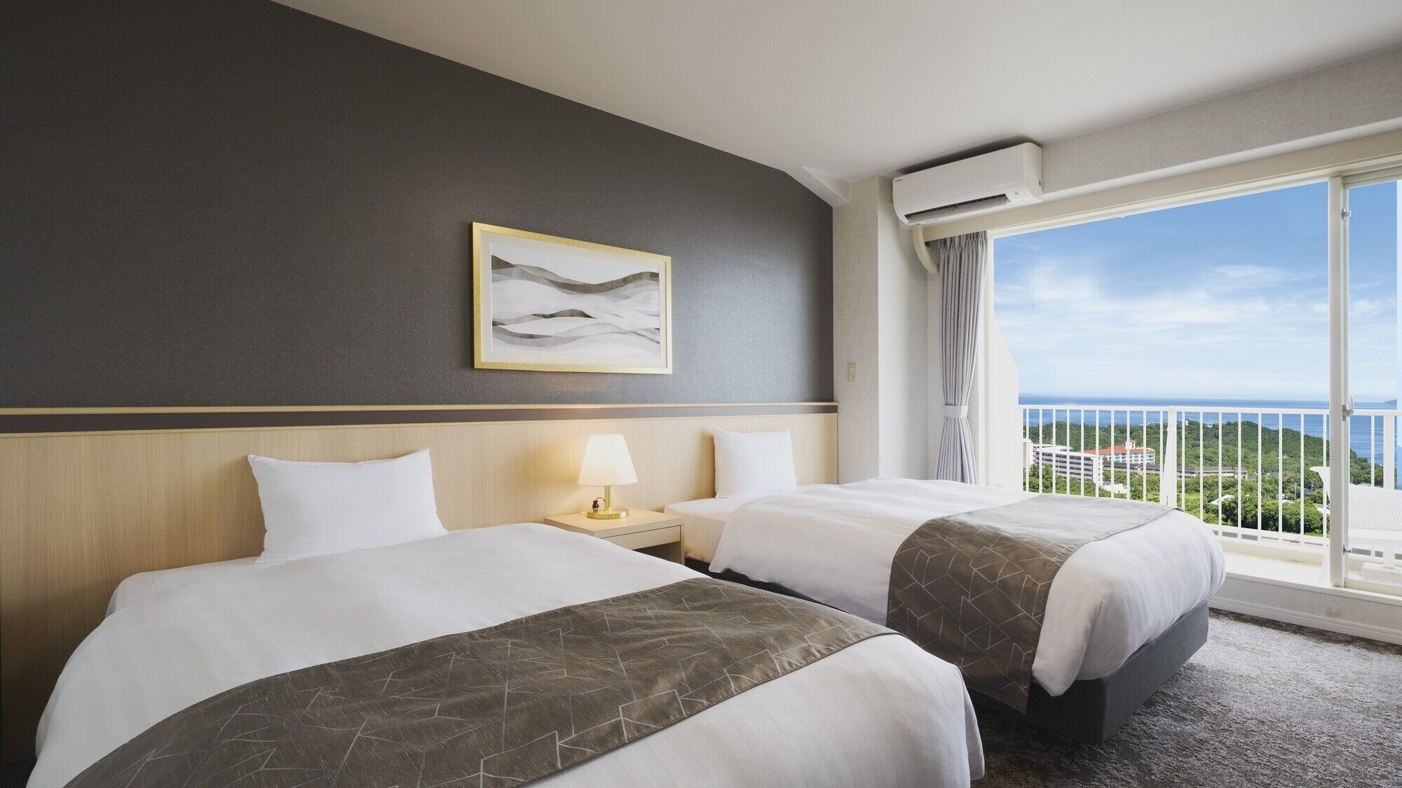Een hotelkamer met twee bedden, een nachtkastje met een lamp, een lijst met een afbeelding aan de muur en een balkon met uitzicht.