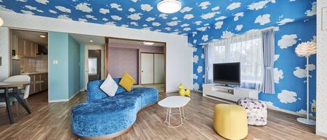A living room with a blue sofa, a yellow ottoman, a white coffee table, and a TV.
