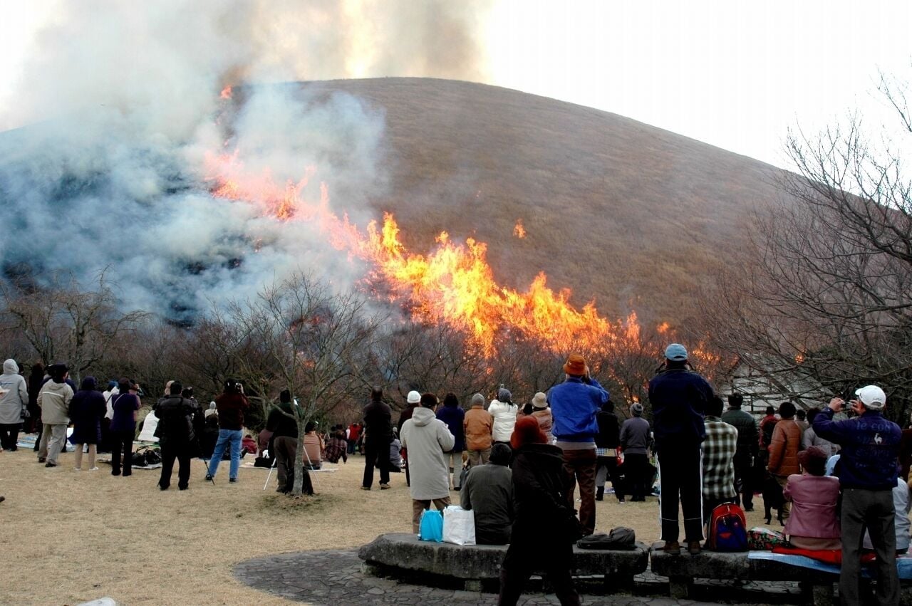 Uma multidão observa um grande incêndio numa colina.