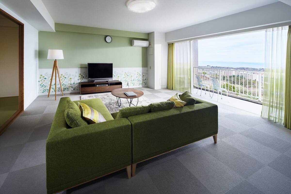 Un salon moderne avec un canapé vert, une table basse et un téléviseur à écran plat posé sur un meuble en bois.
