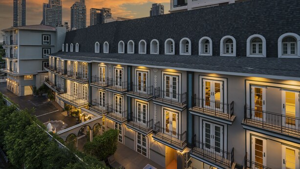 A multi-story hotel with balconies and large windows, set against a city skyline during sunset. -  La Petite Salil Sukhumvit Thonglor 1 (Bangkok)