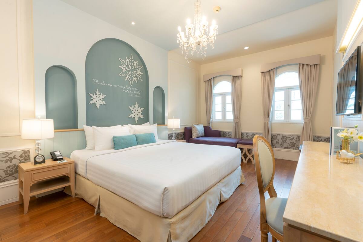 A hotel room with a large bed, a desk, a chair, a chandelier, and a TV.