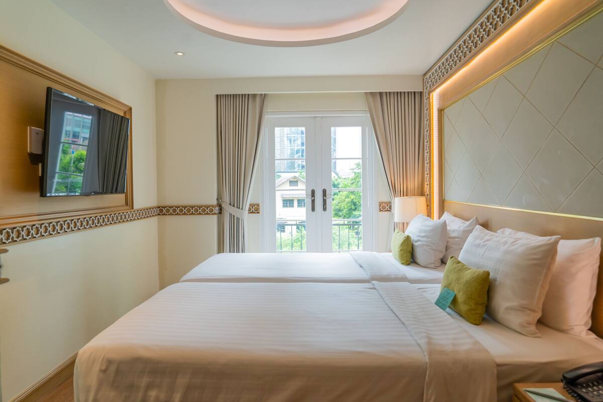 A hotel room with two beds, a television, a balcony with curtains, and a decorative wall panel.