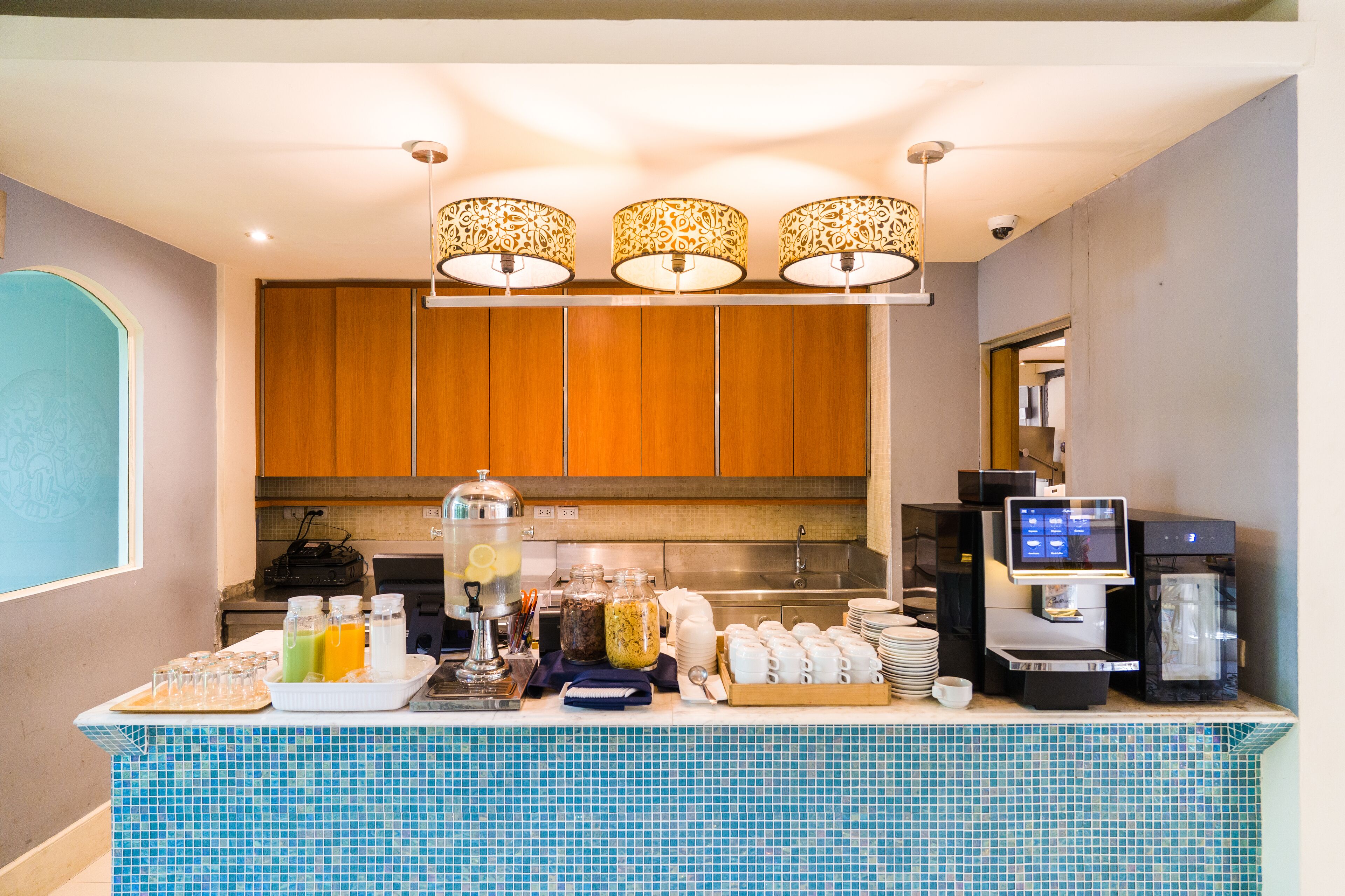 A hotel breakfast area with a coffee machine, a self-service beverage station, and a variety of food and drink options.